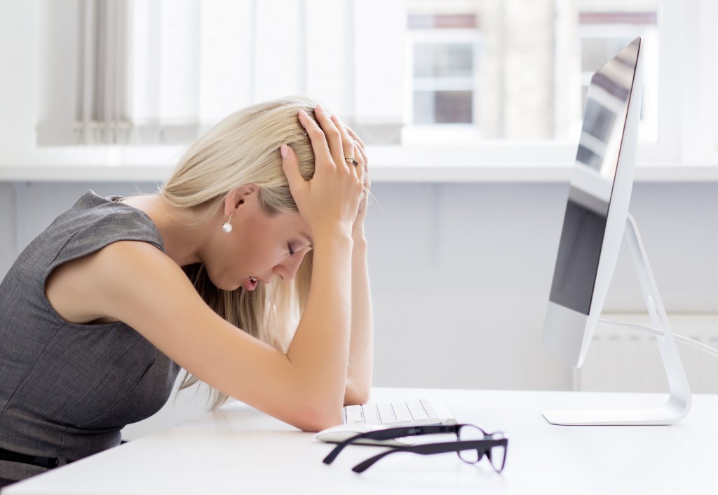 Blond woman getting stressed in front of desktop computer