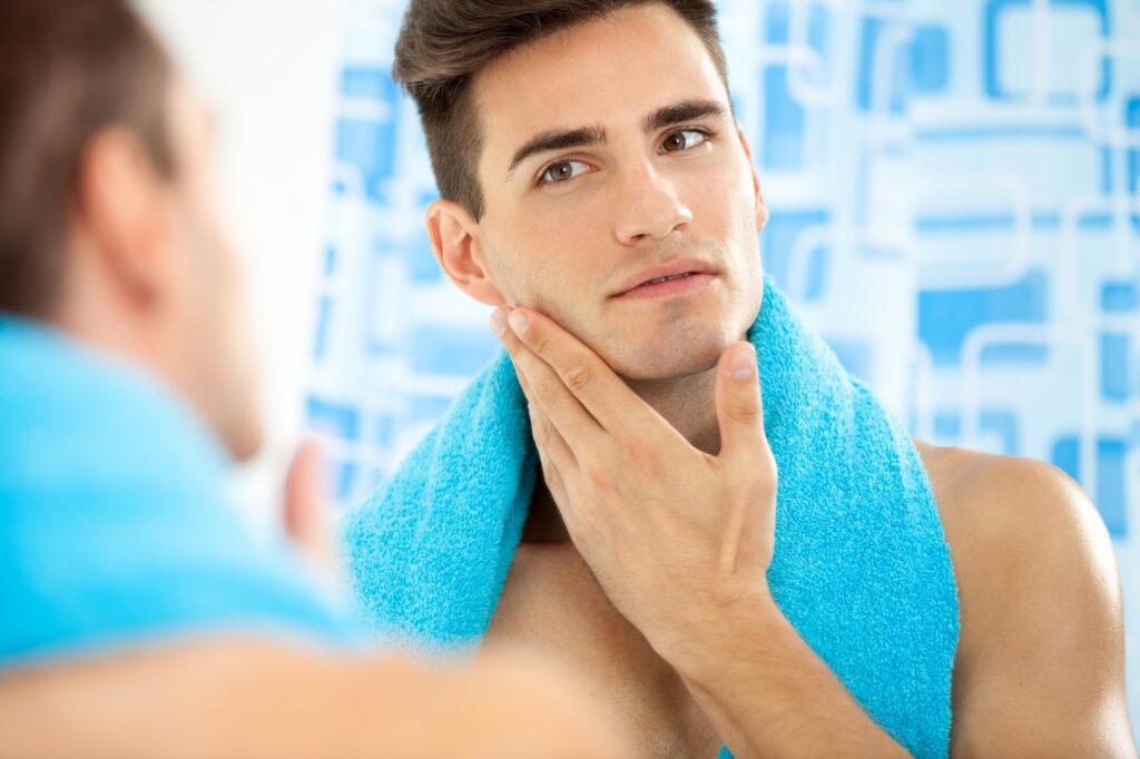 Man checking his face on a mirror after applying moisturizer